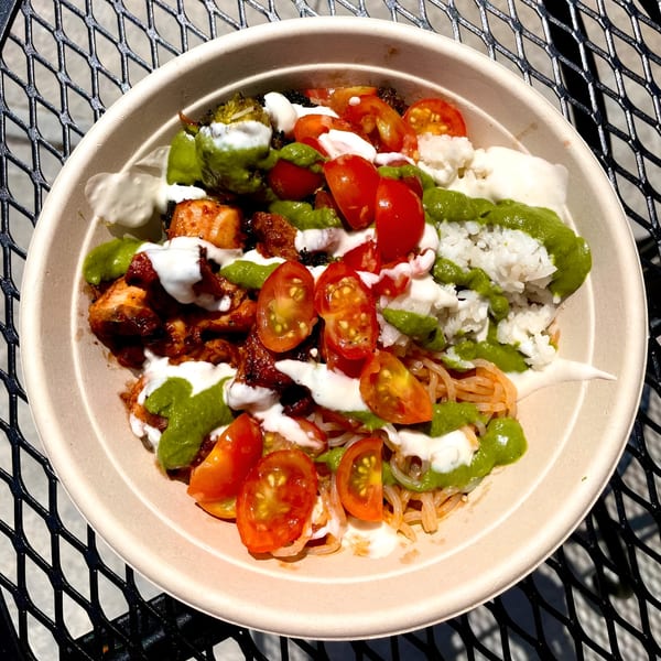 A Fork 'N' Bowl healthy bowl with chicken, rice, tomatoes, and green and white sauces.