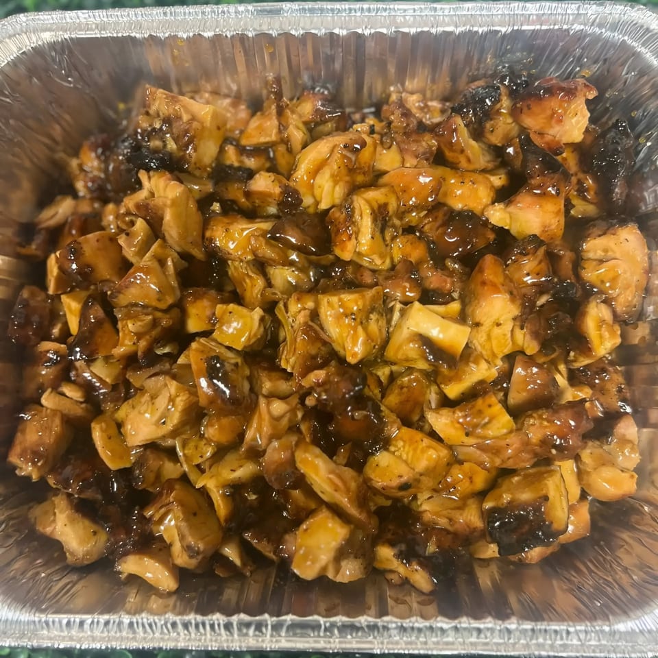Close-up of diced chicken pieces coated in a dark, glossy sauce, served in a foil container.