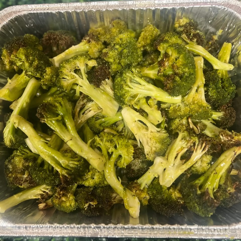 Roasted broccoli florets with seasoning in a silver foil container, ready for a healthy meal.